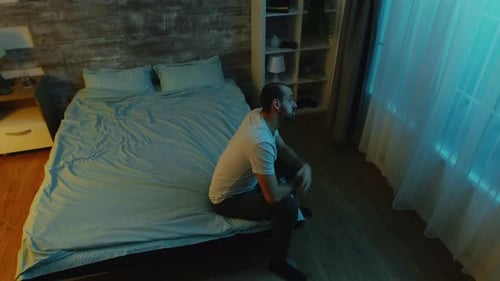 Man Sitting on Bed in Blue Room at Night