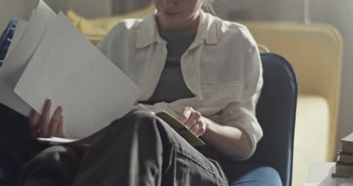Woman Reads Through Papers and Writes in Notebook