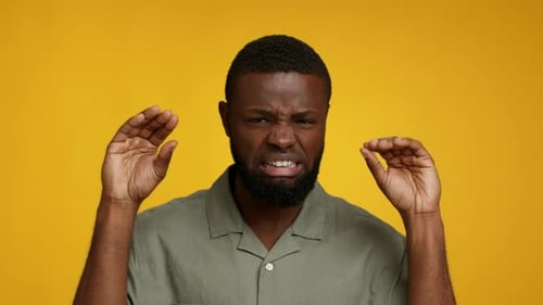 Man Squeezing Hands in Frustration on Yellow Backdrop