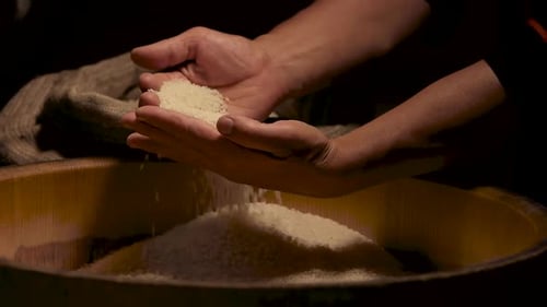 Hands Sifting Rice into Wooden Bowl