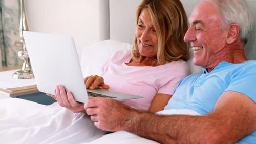 Mature Couple Using Laptop Together in Bed
