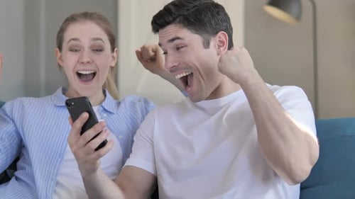 Happy Couple Celebrating While Looking at Smartphone Together