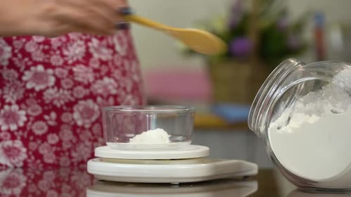 Woman measuring flour with wooden spoon in kitchen