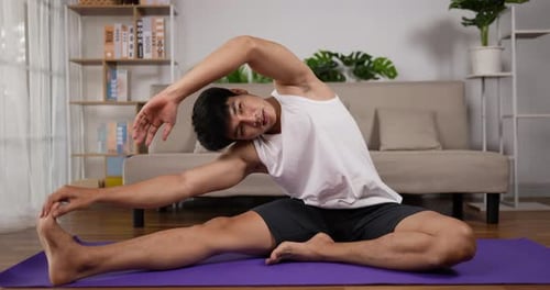 Young Man Stretching on Yoga Mat Indoors