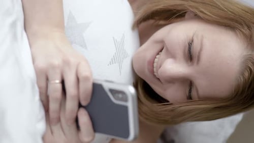 Woman Smiling and Using Her Phone in Bed