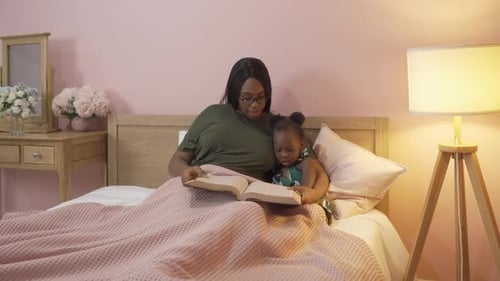 Woman Reading Book to Child in Bed