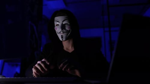 Masked Hacker Typing on Computer Keyboard at Night