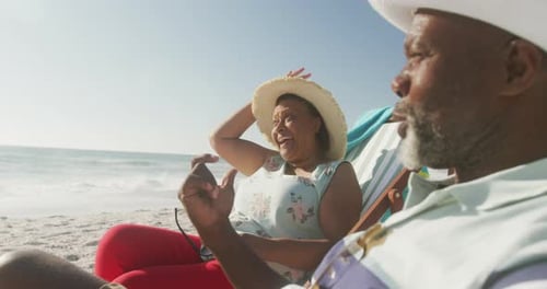 Smiling senior african american couple lying on sunbeds on sunny beach