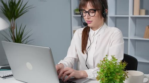 Woman with Headset Typing on Laptop at Desk