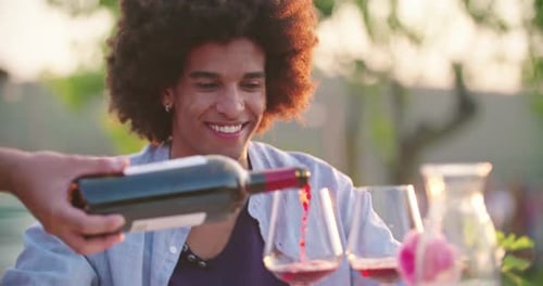 Kellner öffnet die Weinflasche und gießt Rotwein in ein Glas, während die Leute reden, essen, trinken
