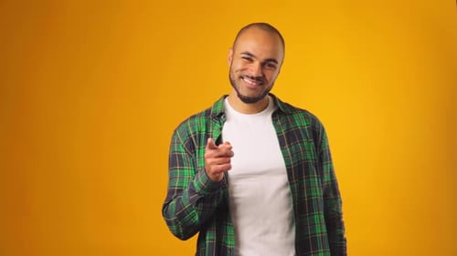 Fröhlicher Afroamerikaner, der vor gelbem Hintergrund lächelt und auf dich zeigt