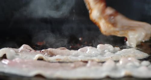 Bacon Sizzling on Grill with Chopsticks Close Up
