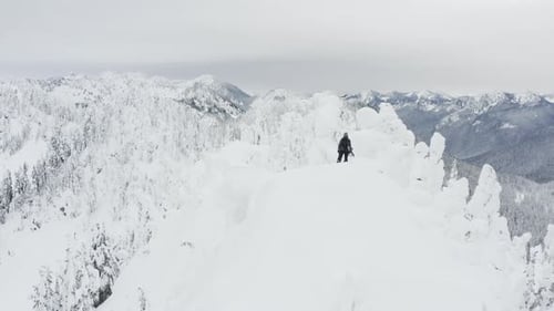 Drone View Flying Around Snowboarder At Mountain Top Of Peak In Mountain Range