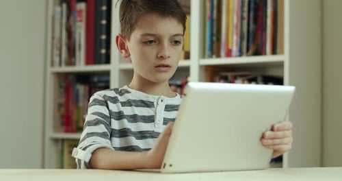 Boy Using Tablet in Front of Bookshelf