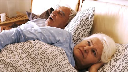 Homme ronflant et femme se couvrant les oreilles en dormant sur le lit
