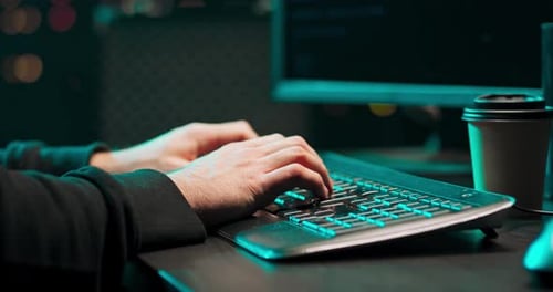 Close-up de mãos de um jovem hacker do sexo masculino escrevendo malware em um teclado de computador em