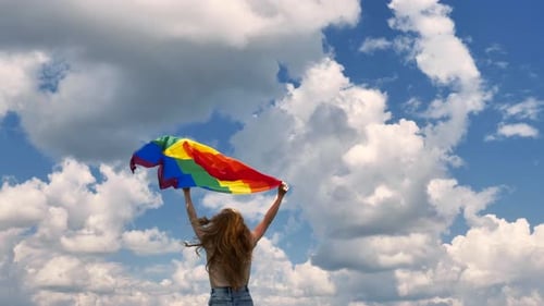 Girl Waving Rainbow Flag in Open Sky