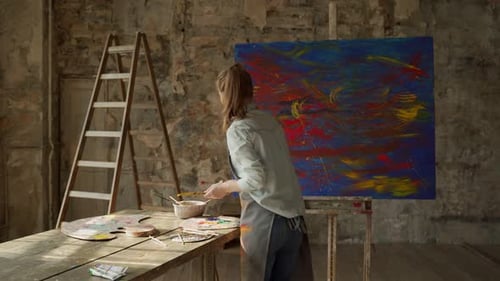 Woman Artist Holding Paint Brush on Large Canvas in Art Studio
