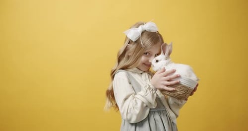 Child Holding Adorable Rabbit in Basket on Yellow Background