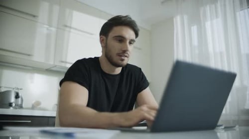 Young Adult Typing on Laptop in Bright Kitchen