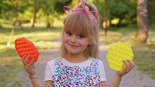 Smiling Girl Holding Pop Toys in Sunny Park