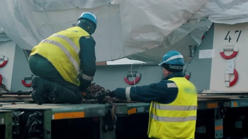 Frachtschifffahrt - Männerarbeiter befestigen die Ladung am LKW