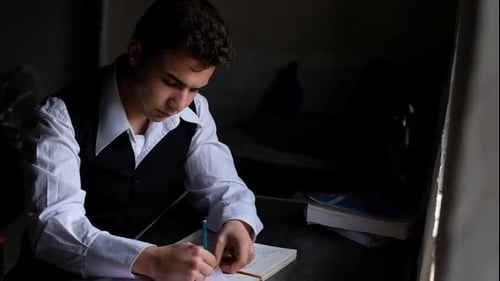 Young Adult Writes in Notebook at Desk