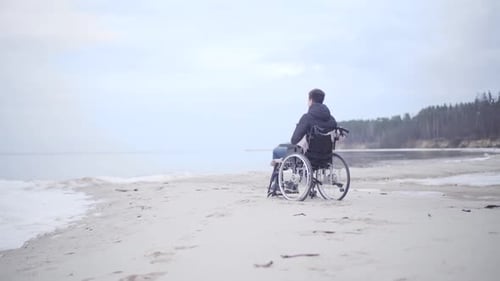 Wide Shot of Young Disabled Caucasian Man in Wheelchair on Autumn River Bank. Brunette Handicapped