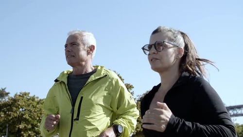 Couple of Happy Older Runners Jogging Down Street