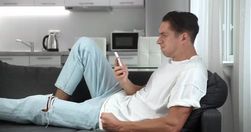 Surprised man lying on couch looking at phone