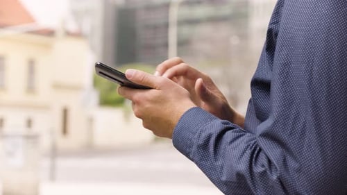 A Man Works on a Smartphone in an Urban Area Closeup a Street in the Blurry Background