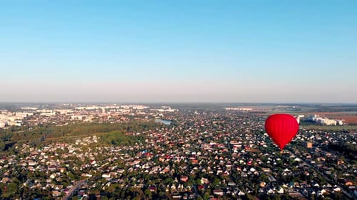 A beautiful red balloon flies in the evening over the river and the city.