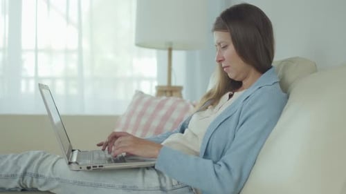 Woman Works on Laptop While Relaxing on Couch
