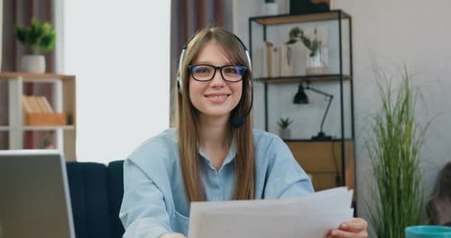 Smiling Woman with Headset Holding Paper at Desk