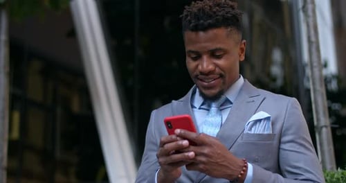 Cheeerful Afro American Guy in Suit and Tie Communicating and Smiling While Typing on Phone Screen