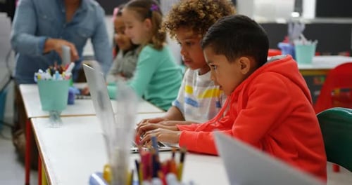 Seitenansicht von Schülern gemischter Abstammung, die im Klassenzimmer auf einem Laptop lernen 4k