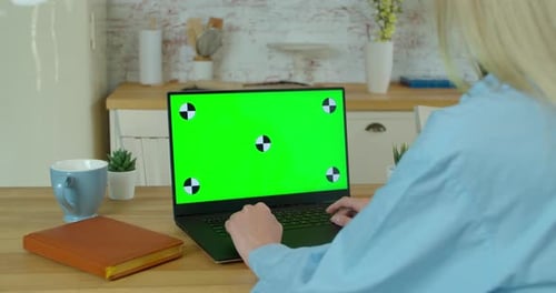 Young Woman at Home Works on a Laptop Computer with Green Mock-up Screen. Working at Home in