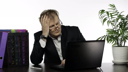 Müder zerzauster Geschäftsmann arbeitet hart im Büro am Laptop am Schreibtisch