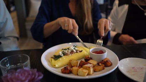 Woman uses knife and fork to cut an omelet and put it into her mouth.