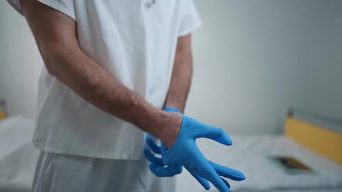 Unrecognizable Doctor Putting on Blue Disposable Surgical Gloves Standing in Hospital Ward Indoors