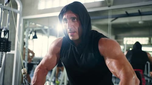 4K Caucasian man bodybuilder pulling weight lifting machine at gym.