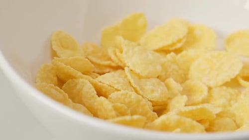 Yellow Corn Flakes Pouring into White Bowl