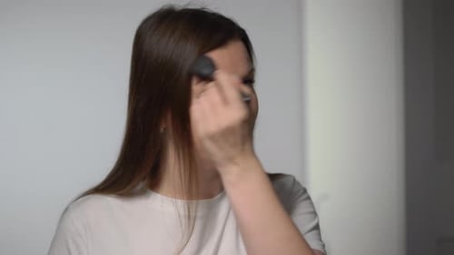 Woman Applies Makeup with Brush in Bright Setting