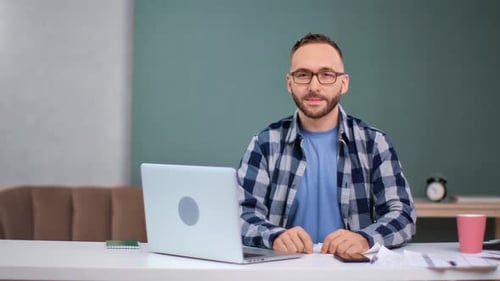 Porträt eines gutaussehenden Mannes mit Brille, der am Tisch vor dem Laptop posiert