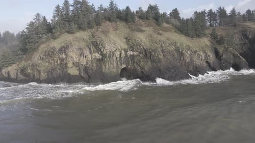 Brown water ocean waves crash up against the rough rugged Washington coastline, aerial track