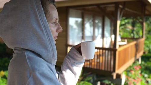 Side View o Caucasian Girl Standing on a Balcony with the Jungle View Welcoming New Day with a Cup