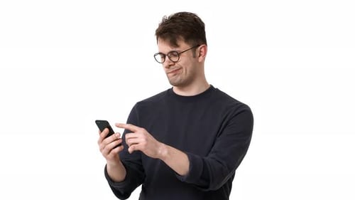 Porträt eines glücklichen Mannes aus den 20ern mit schwarzem Sweatshirt und Brille, der auf dem Smartphone im Internet surft