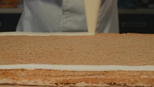 Gebackener Biskuitkuchen für den gesamten Rahmen. Ein cooler Konditor trägt Sahne rund um den Rand auf
