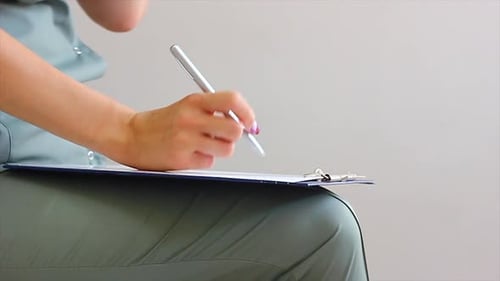 Young Doctor of Caucasian Nationality in a Dark Green Coat Writes with a Pen in a Notebook Closeup