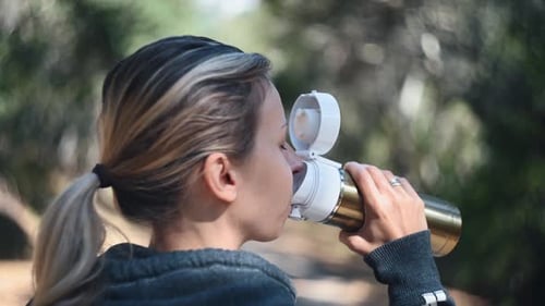 Woman Drinks Water from Metal Bottle Outdoors